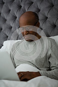 Smiling senior man using laptop on bed