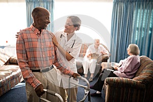 Smiling senior man with walker looking at female doctor against window