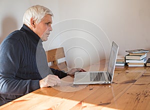 Smiling senior man  wave to camera having video call on laptop, happy elderly male  sit  at home talk using modern technologies
