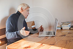 Smiling senior man  wave to camera having video call on laptop, happy elderly male  sit  at home talk using modern technologies