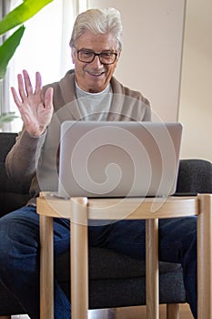 Smiling senior man waving hand to laptop