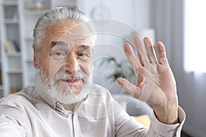 Smiling senior man waving hello in a bright room