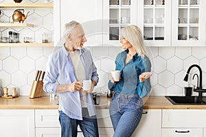 Smiling senior man and woman drinking coffee together in modern kitchen interior