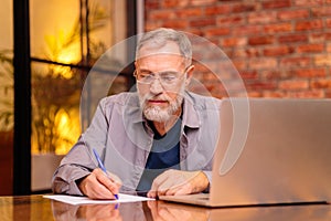 Smiling senior middle aged man in glasses working on laptop at home