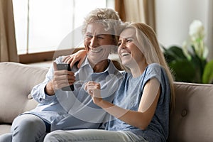 Smiling senior mom and adult daughter have fun using cellphone