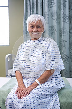 Smiling senior patient sitting on bed in hospital