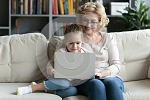 Smiling senior 60s granny use laptop with small granddaughter photo