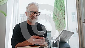 Smiling senior texting smartphone in cafe closeup. Successful bearded man browse