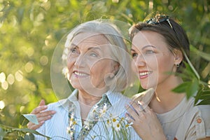 Smiling senior woman with adult daughter with flowers in park