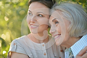 Smiling senior woman with adult daughter with flowers in park