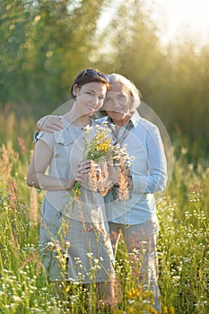 Smiling senior woman with adult daughter with flowers in park