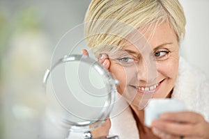 Smiling senior woman applying anti-aging cream