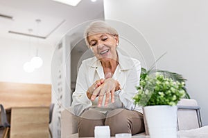 Smiling senior woman applying anti-aging hand lotion . Happy mature woman using cosmetic cream to hide wrinkles. Lady using day