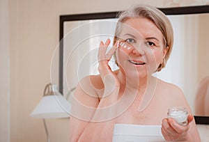 Smiling senior woman applying anti-aging lotion to remove dark circles under eyes.