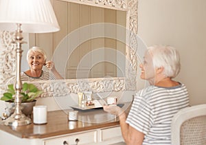 Smiling senior woman applying makeup in a mirror at home