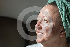 Smiling senior woman applying moisturizing anti aging face cream or lotion. Skin and face care concept. Modern granny.