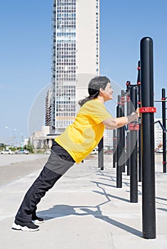 Smiling senior woman doing push ups outdoors on the sports ground bars