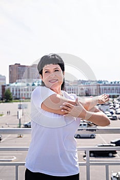 Smiling senior woman doing stretching outdoors on urban background