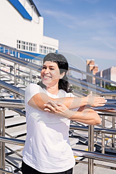 Smiling senior woman doing stretching outdoors on urban background