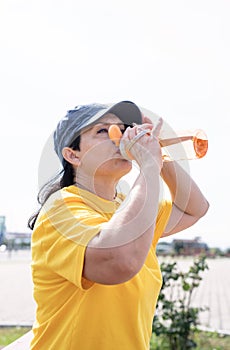 Smiling senior woman drinking water after workout outdoors on the sports ground