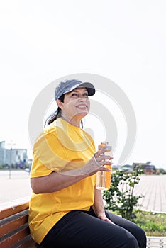 Smiling senior woman drinking water after workout outdoors on the sports ground