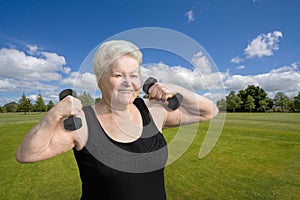 Smiling senior woman exercising with dumbells in park photo