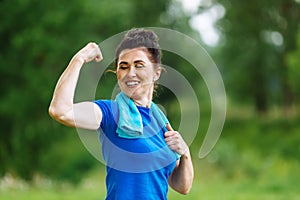 Smiling Senior woman flexing muscles outdoor in park. Elderly female showing biceps. Heathy life style concept