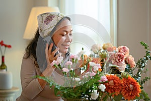 Smiling senior woman flower shop owner taking orders from client on mobile phone. Floristry and small business concept