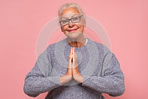 Smiling senior woman in glasses holding hands in prayer show hope and belief, say Namaste