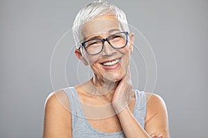 Smiling senior woman with gray hair and glasses posing in front of gray background