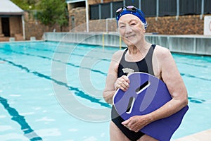 Smiling senior woman holding kickboard at poolside