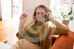 Smiling senior woman holding red apple and enjoying mobile phone call
