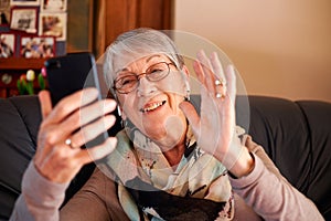 Smiling Senior Woman At Home Waving As She Makes Video Call To Family On Mobile Phone