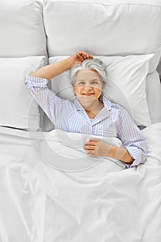 smiling senior woman lying in bed at home bedroom