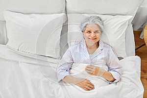 smiling senior woman lying in bed at home bedroom