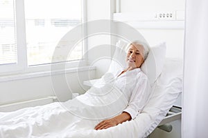 Smiling senior woman lying on bed at hospital ward