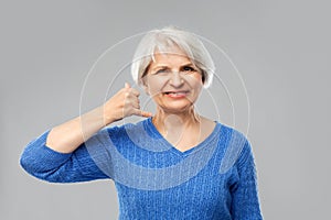 Smiling senior woman making phone calling gesture