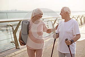 Smiling senior woman with mat cheers up man with poles for Nordic walking on footbridge