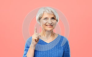 Smiling senior woman pointing finger up over pink