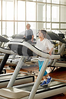 Smiling senior woman running on treadmill in gym.