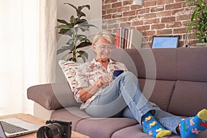 Smiling senior woman sitting on sofa at home using mobile phone and laptop