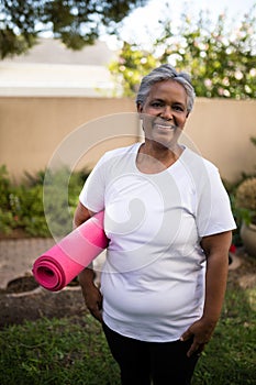 Smiling senior woman standing with exercise mat at park