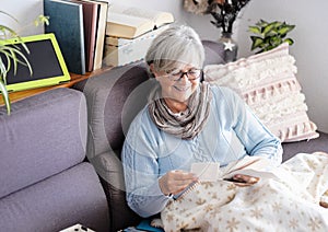 Smiling senior woman stay home to prevent covid-19 contagion sitting on sofa looking at old photographies memories of the past
