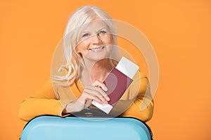 Smiling senior woman with suitcase and passport.