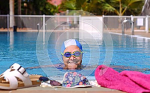 Smiling senior  woman swimm into the swimming pool with swimming goggles and cap  - active retiree enjoying healthy lifestyle