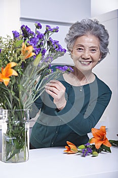 Smiling senior woman touching a bouquet of flowers in the kitchen, portrait