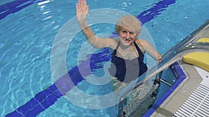 Smiling senior woman waves hand in the swimming pool
