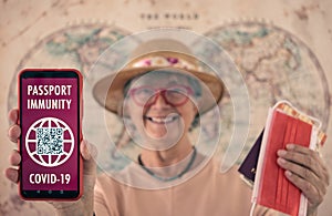 Smiling senior woman wearing straw hat shows health passport app for people vaccinated against coronavirus, ready to travel
