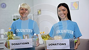 Smiling senior and young volunteers holding food donation boxes looking camera