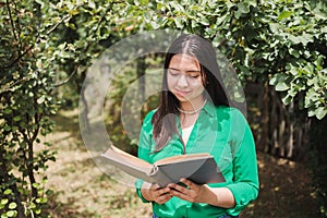 Smiling serene young woman reading a book in the greenery of the field. Benefits of reading